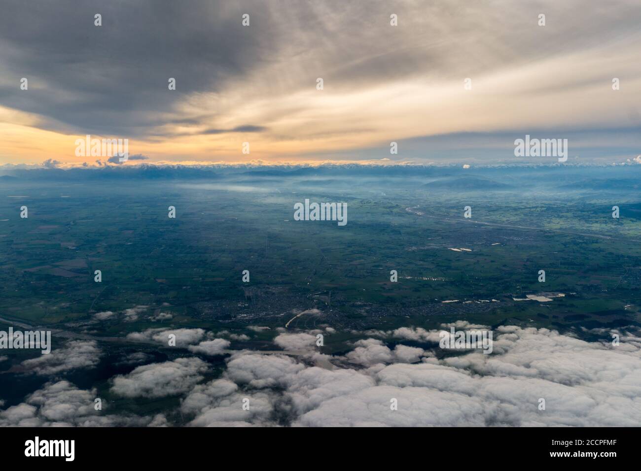 Flying over Christchurch area with views of the east coast of New Zealand's South Island the clouds cover the sunset. Just a glimpse of the sun comes Stock Photo