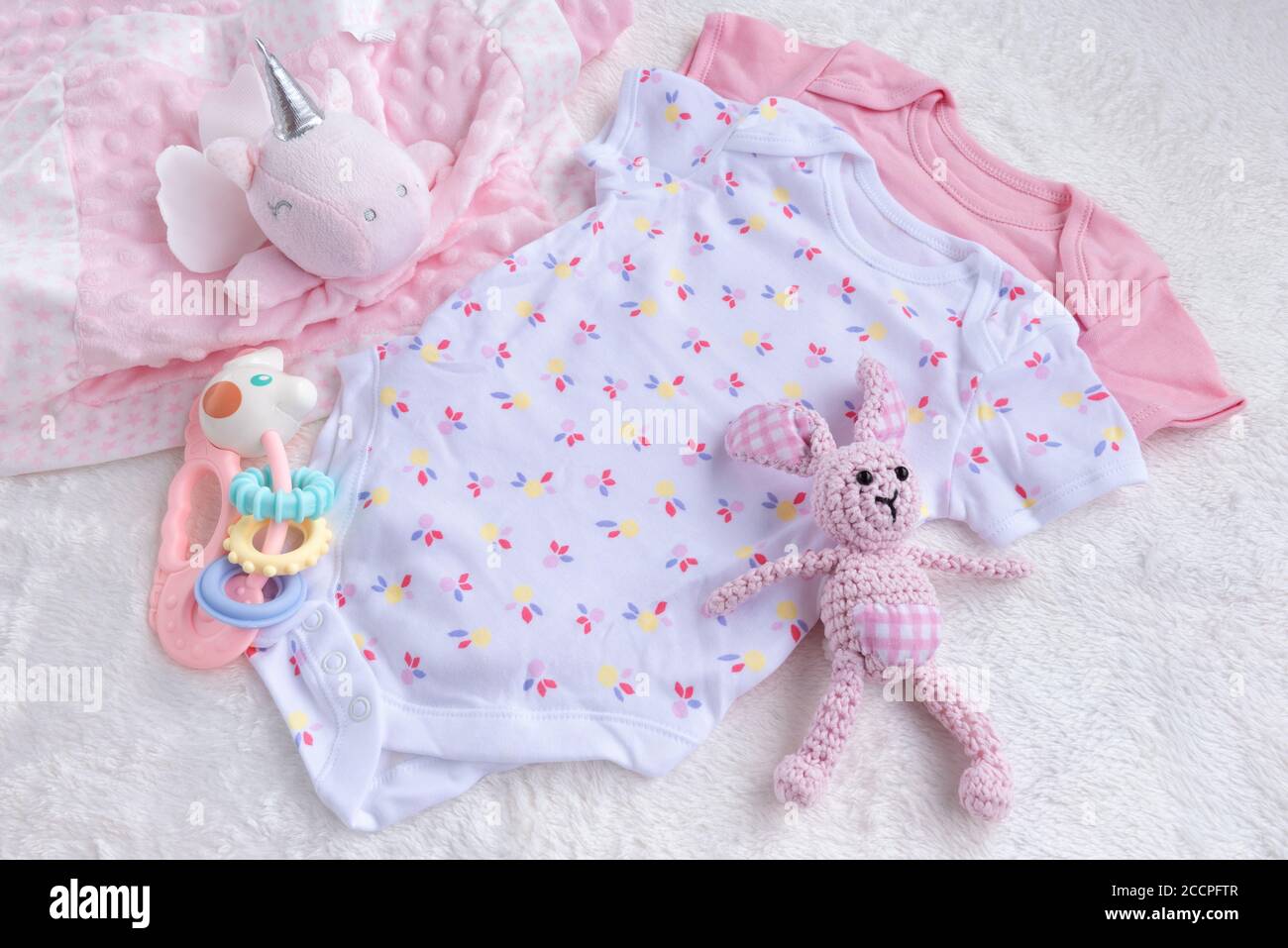 Baby Mockup. Bodysuits for baby girl And Rattle Toy On A White Fur Carpet. Newborn Baby Concept. Baby Girl Clothes Set. Stock Photo