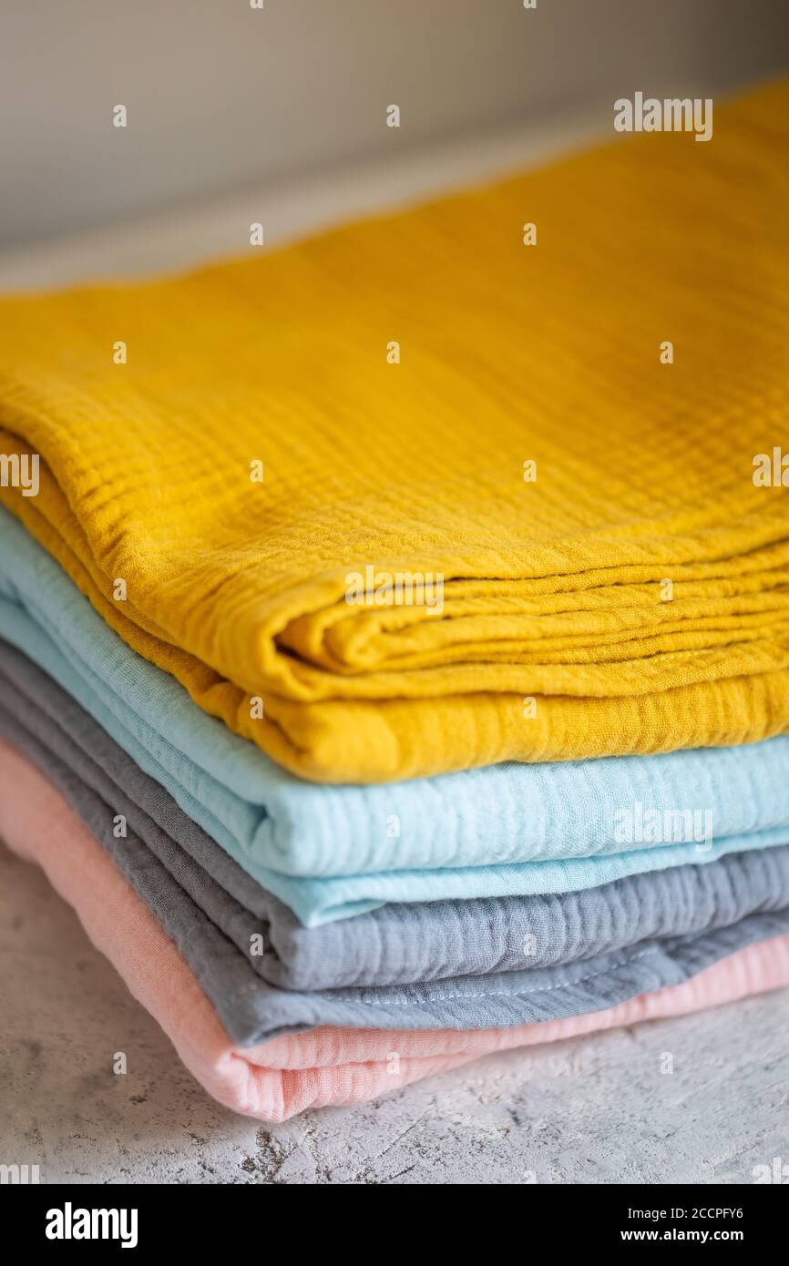 Pink, blue, mustard, grey muslin fabrics, diapers on a white background closeup. Beautiful pile of fabrics on the table Stock Photo