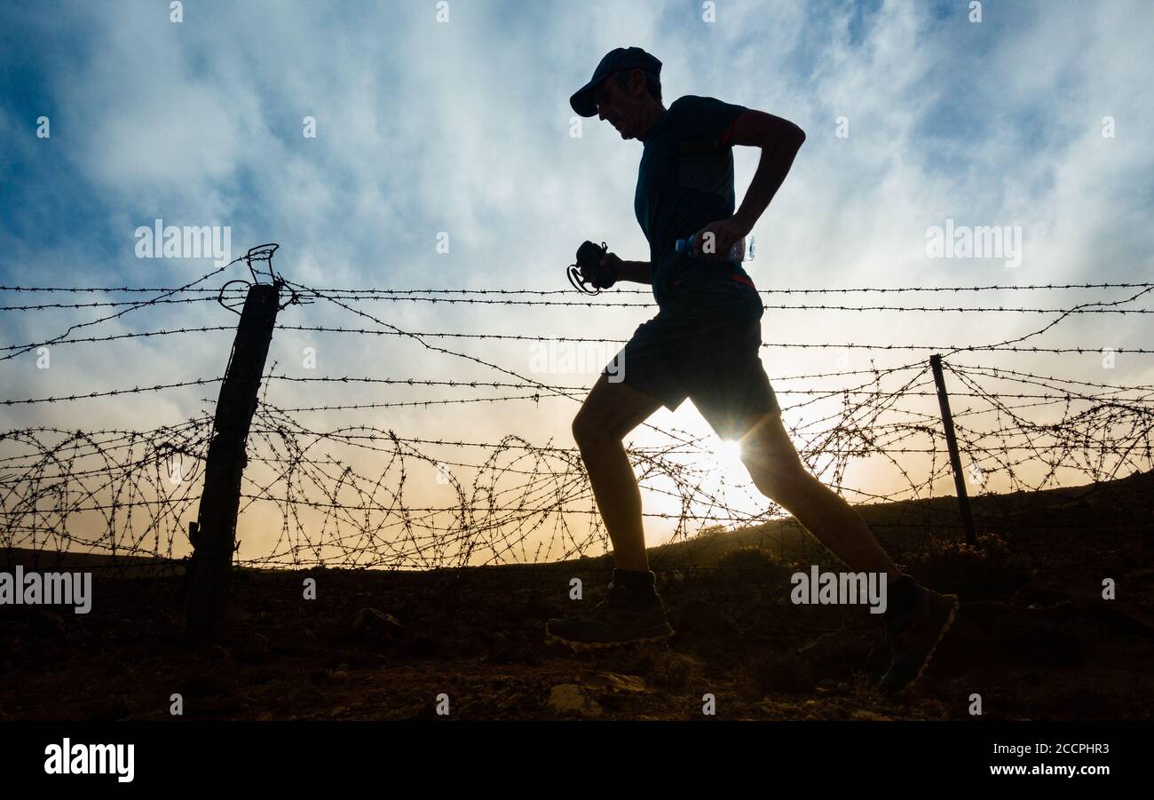 Las Palmas, Gran Canaria, Canary Islands, Spain. 24th August, 2020. A trail runner runs past military base fence at sunrise on Gran Canaria as Covid 19 cases continue to rise in the Canary Islands and the rest of Spain. More new Coronavirus cases have been recorded in the month of August on Gran Canaria than during the months of March to August combined. More than 100 of the new cases have been traced to a Disco in the capital Las Palmas. Credit: Alan Dawson/Alamy Live News Stock Photo