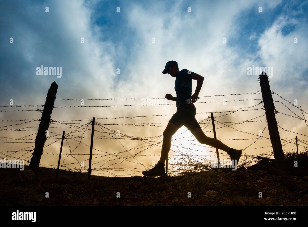 Las Palmas, Gran Canaria, Canary Islands, Spain. 24th August, 2020. A trail runner runs past military base fence at sunrise on Gran Canaria as Covid 19 cases continue to rise in the Canary Islands and the rest of Spain. More new Coronavirus cases have been recorded in the month of August on Gran Canaria than during the months of March to August combined. More than 100 of the new cases have been traced to a Disco in the capital Las Palmas. Credit: Alan Dawson/Alamy Live News Stock Photo