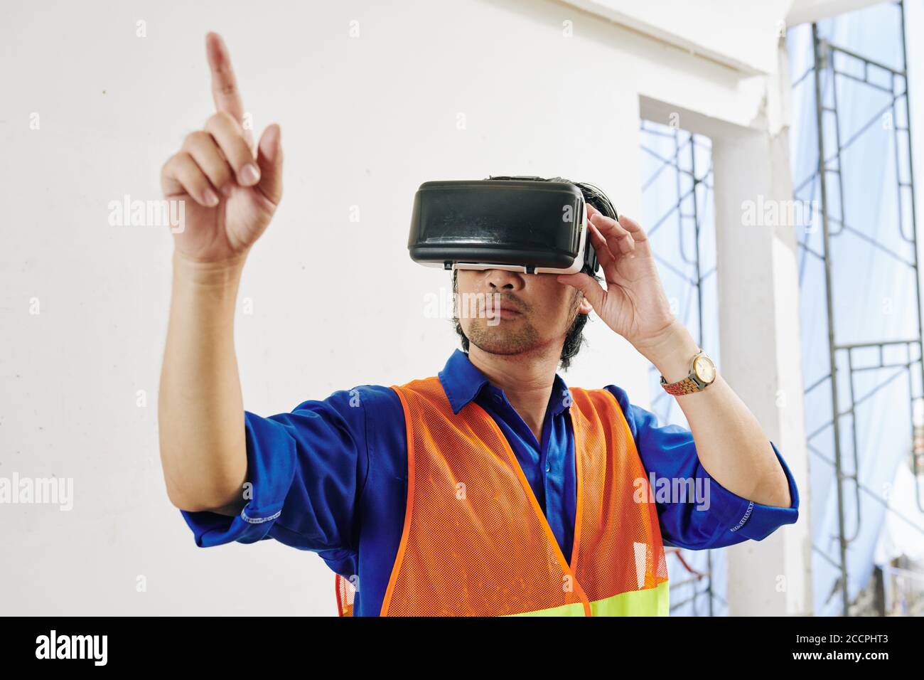 Serious builder in brigh orange vest and headset testing augmented reality application Stock Photo