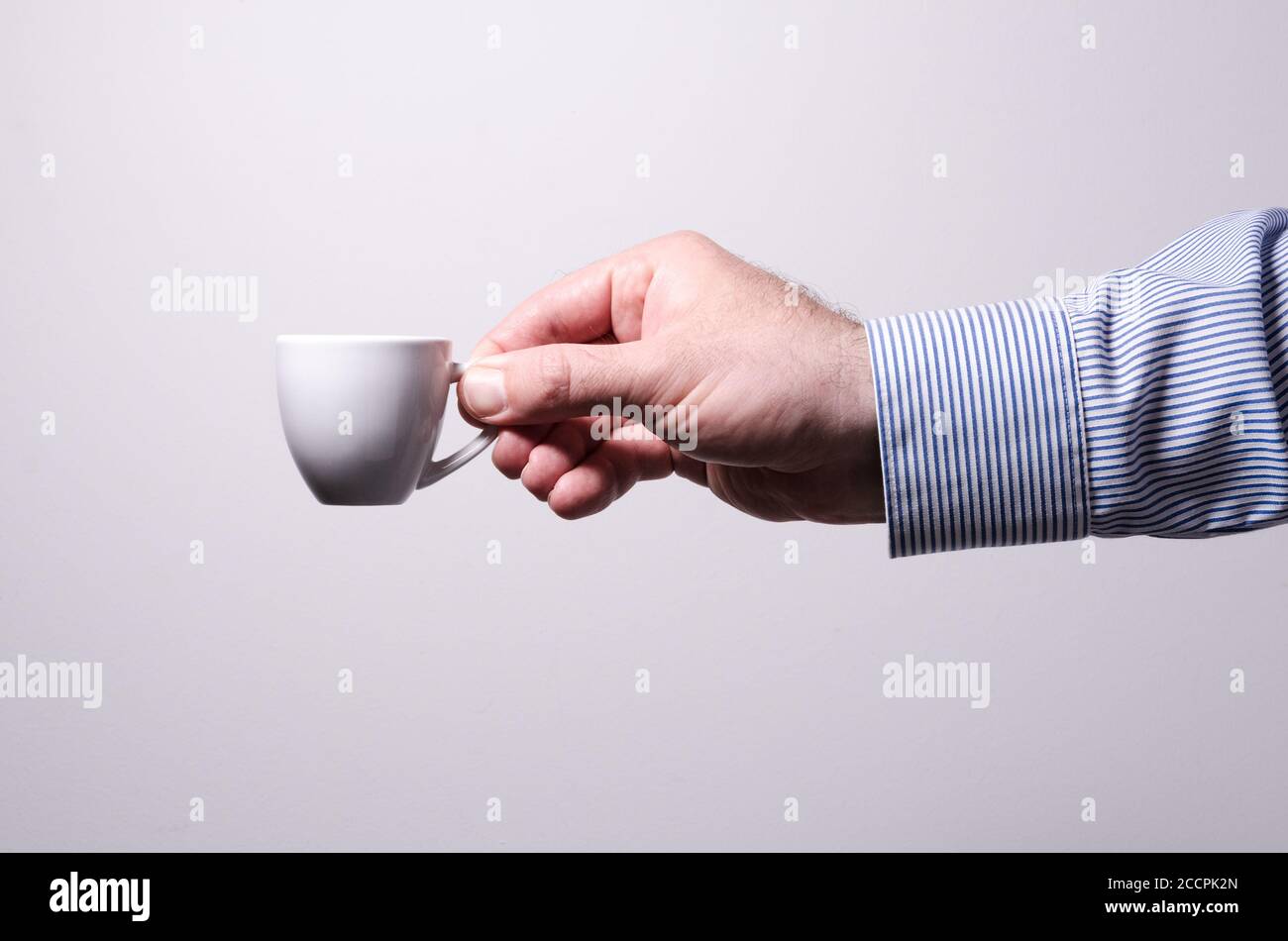 Male hand holding white cup with hot beverage, espresso coffee, against white background, indoors, studio Stock Photo