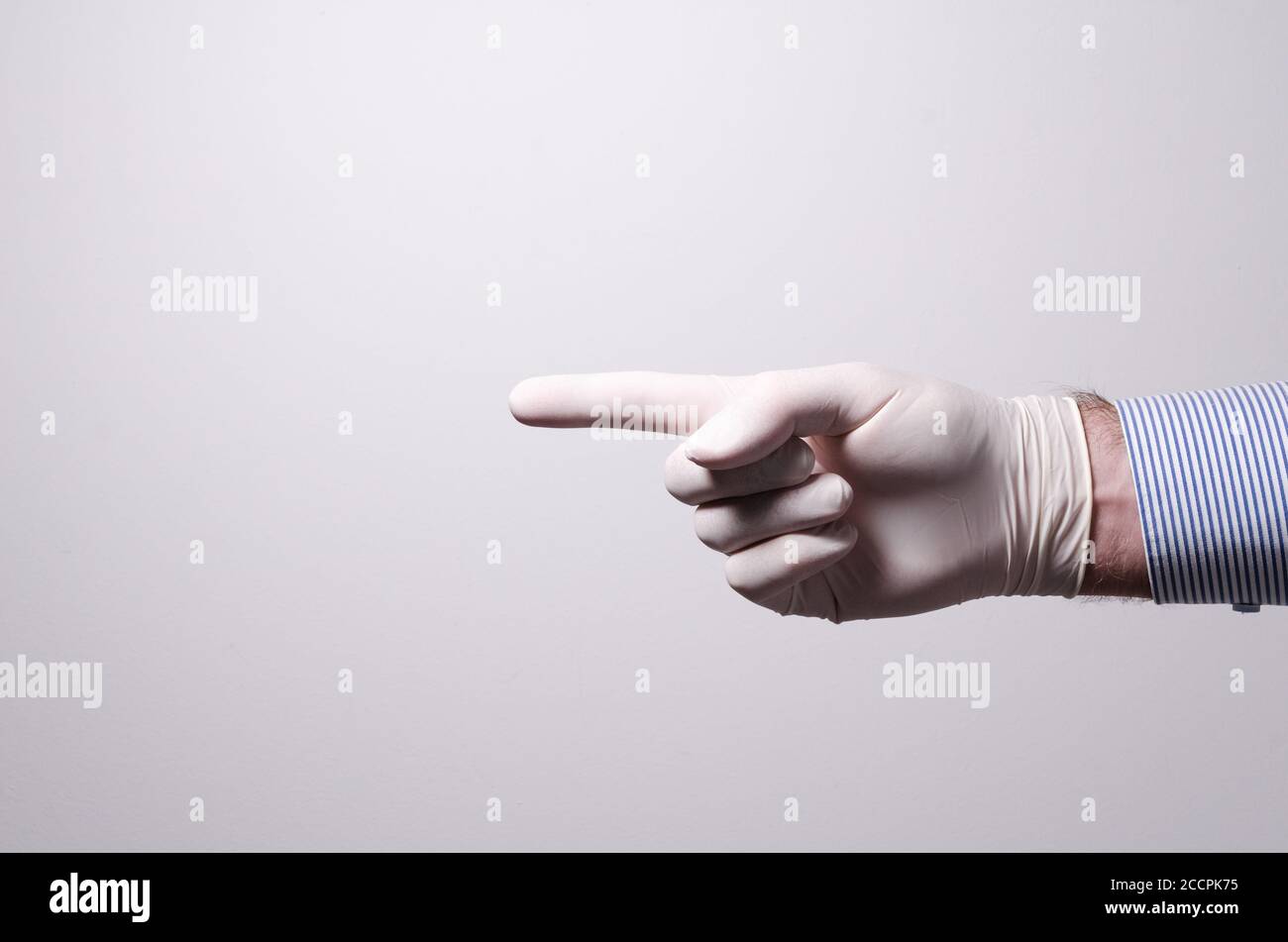 Male hand wearing rubber protective glove, pointing finger, against white background, indoors, studio Stock Photo