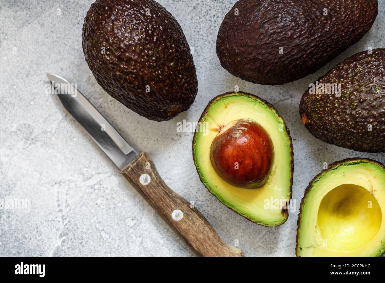 Whole and cut in half ripe organic avocados and a knife on a grey