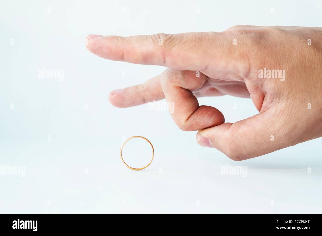 Divorce concept. Male hand kicking wedding ring on white background. Relationship breakup. Unfaithful spouse. Person pulls off the golden ring. Not Stock Photo