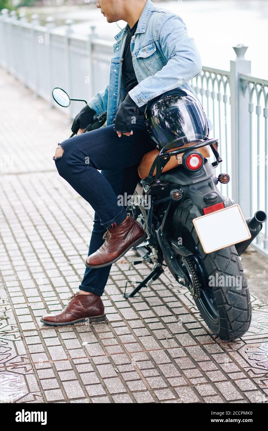 Cropped image of cool young man in leather boots and denim jacket leaning  on his motorbike when standing outdoors Stock Photo - Alamy