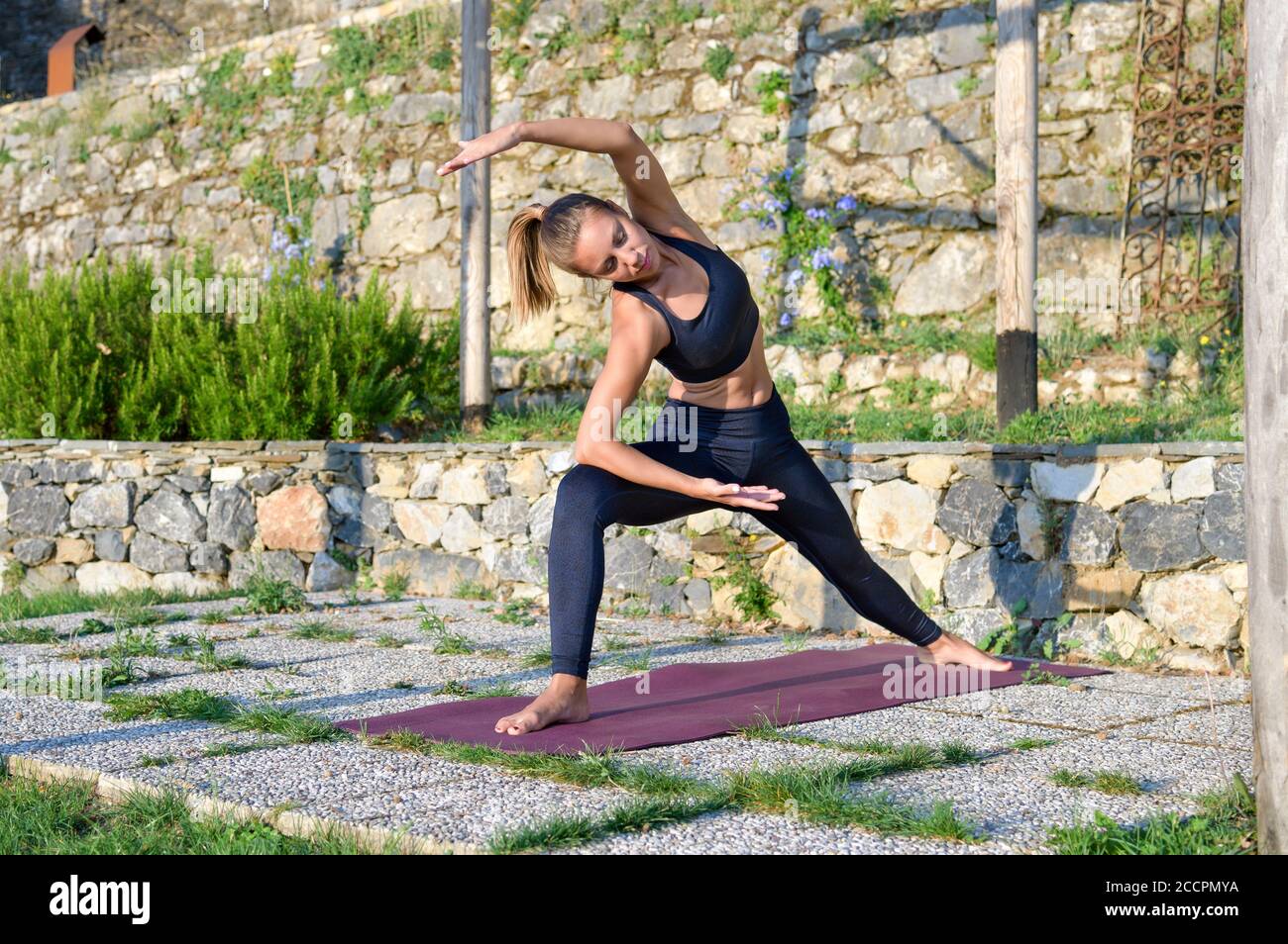 Girl doing an extended side angle yoga pose as she works out outdoors in the garden in a health and fitness concept stretching and toning her muscles Stock Photo