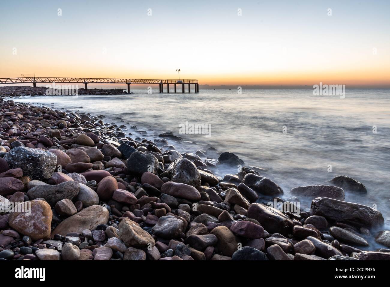 Sunrise from a pebble beach with a walkway to the sea Stock Photo