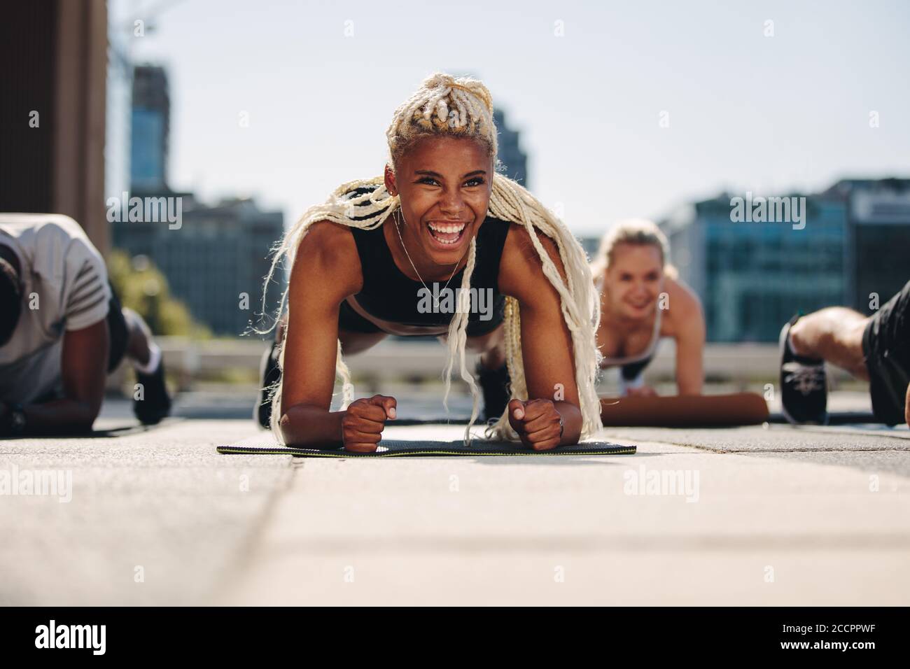 Group of young adults working out together outside in the city. Men and women holding a plank position and smiling. Stock Photo