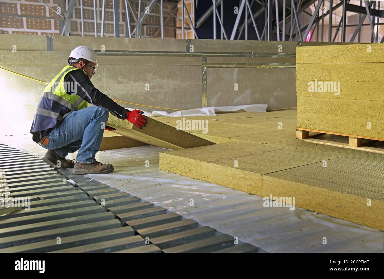 A workman lays insulation slabs in the roof space of a large industrial unit in East London, UK. Stock Photo