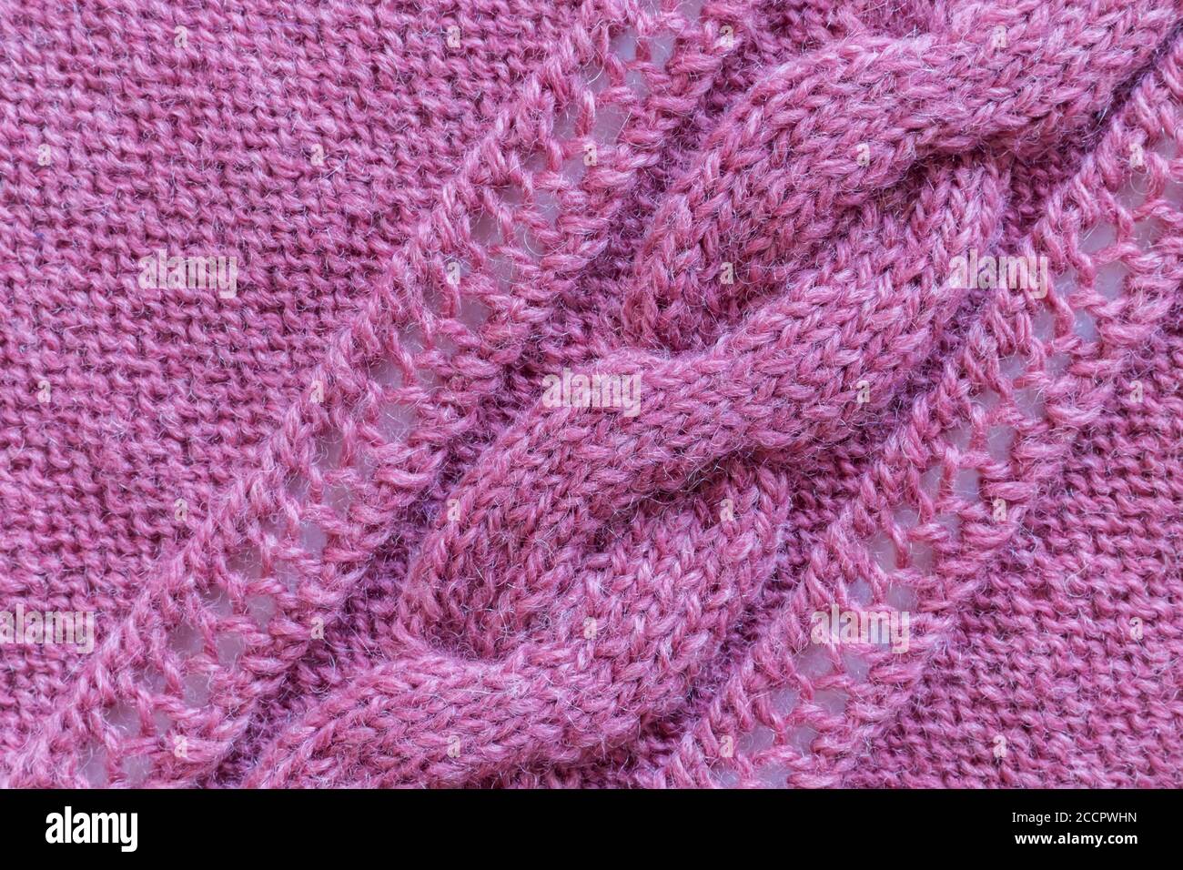 Openwork pattern knitted with needles from pink wool yarn. Stock Photo