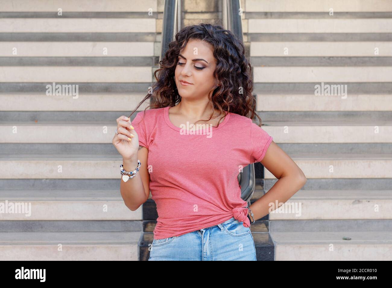 Young women wearing t-shirt and jeans stays near the stairs and touch hairs Stock Photo