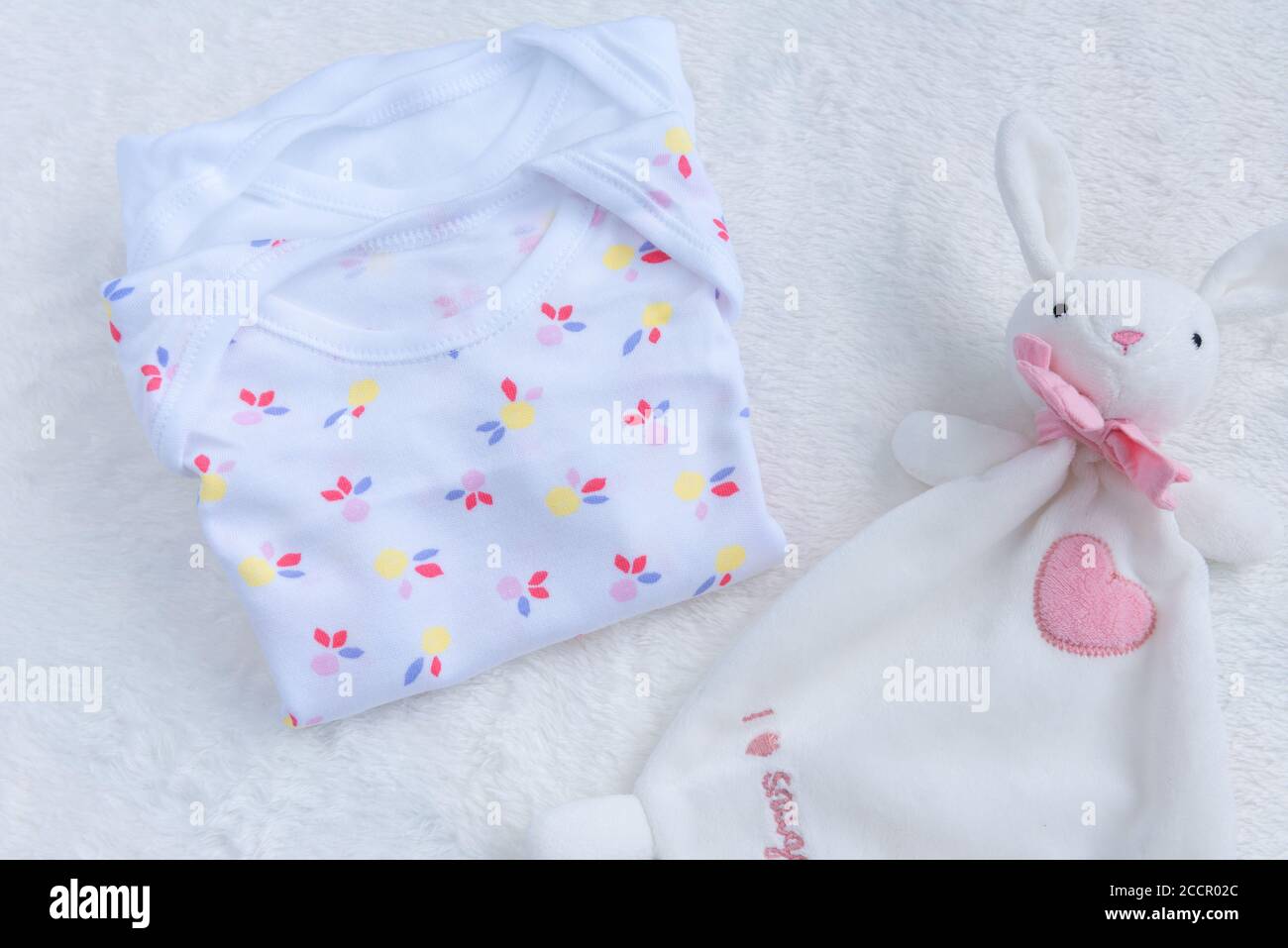 Bodysuits for baby girl and a toy on a white fur carpet. Newborn Baby Concept. Baby Girl Clothes Set. Stock Photo