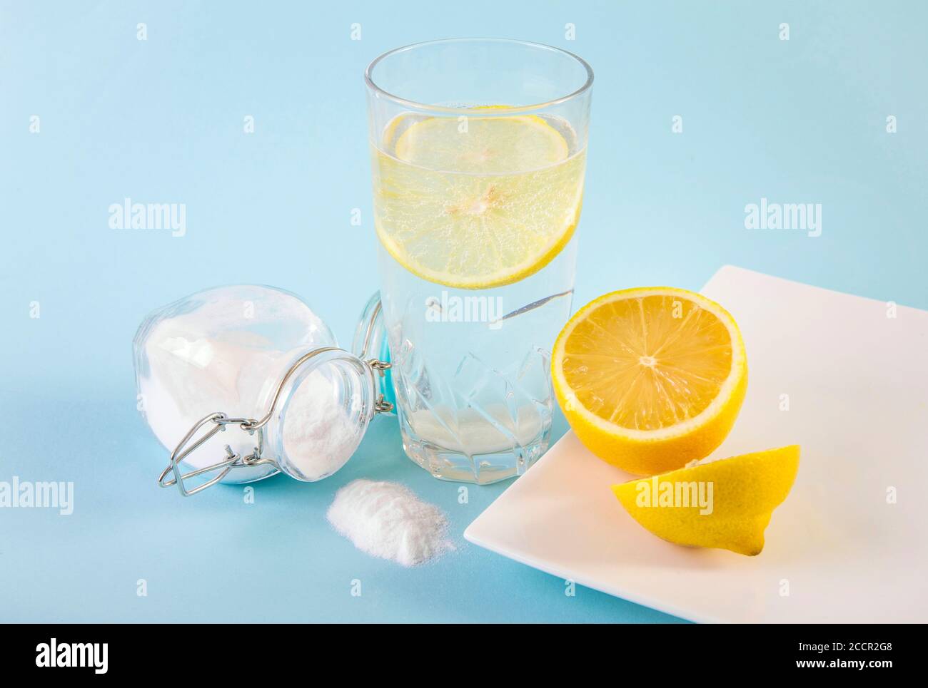 Baking soda in drinking glass with water and lemon juice, health benefits for digestive system concept. Light blue background. Stock Photo