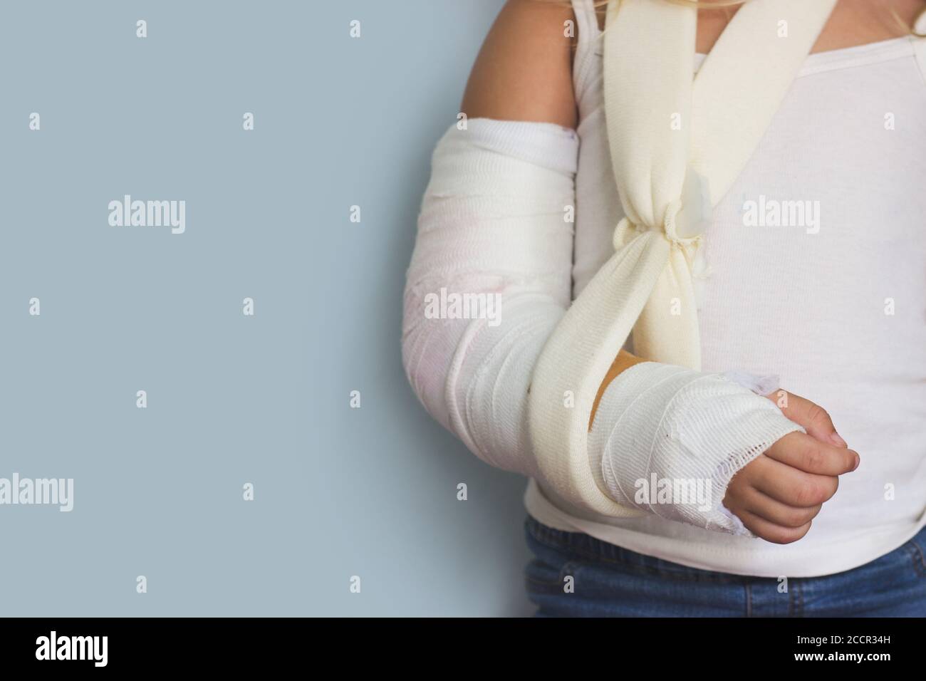 Little girl with broken arm, in plaster, against blue wall, with copy space Stock Photo
