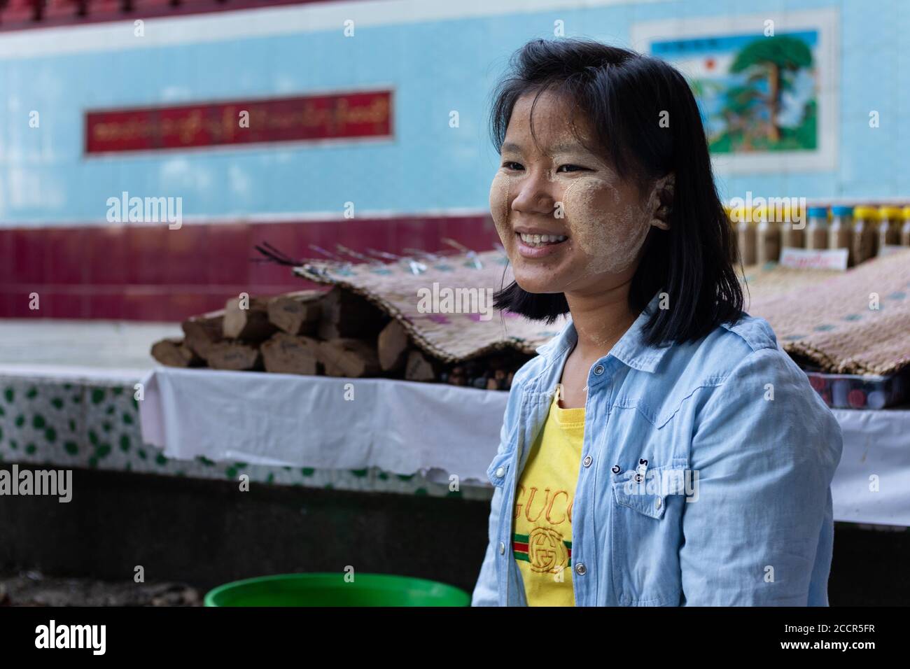Portrait of a female thanaka seller at a buddhist temple. Thanaka paste on face used as cosmetic and mosquito repellent. Smiling burmese girl. Myanmar Stock Photo