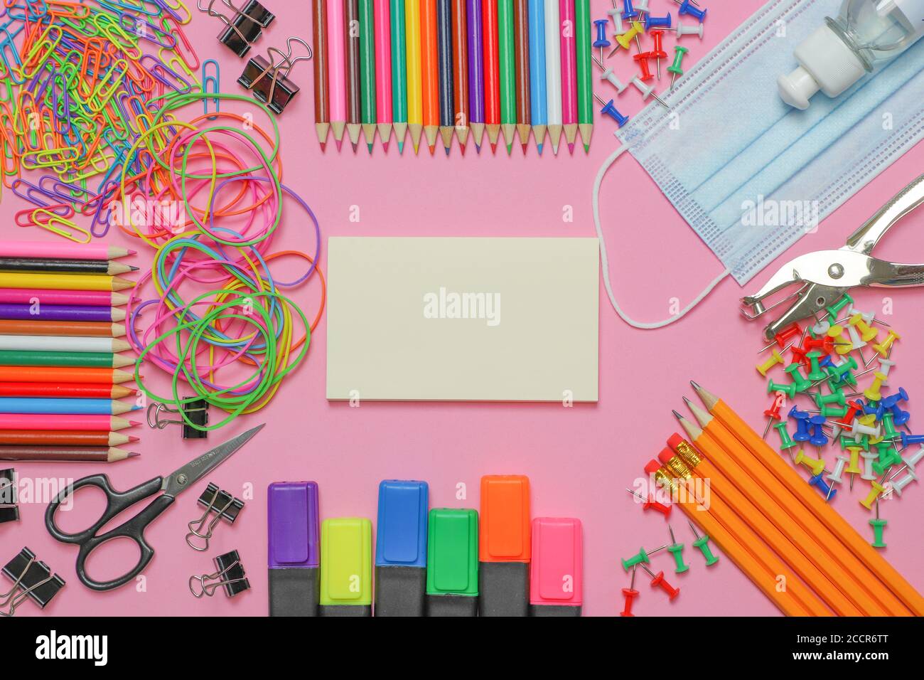 School stationery supplies with medical mask and hand sanitizer on pink background. Back to school and new normal concept. COVID-19 prevention. Stock Photo