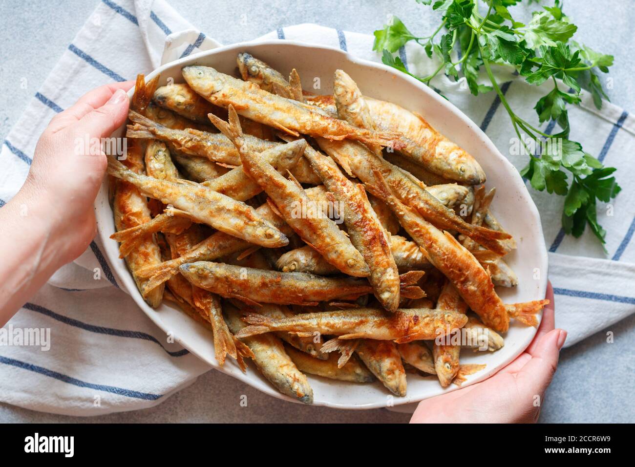 Fried smelt. A woman serves delicious small fish in a white plate. Gourmet appetizer. Selective focus, top view Stock Photo