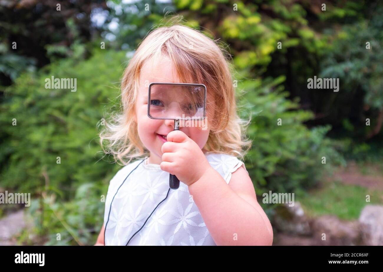 Young child female 3 years old playing outdoors in the woods with a magnifying glass looking for bugs and insects to look at Stock Photo