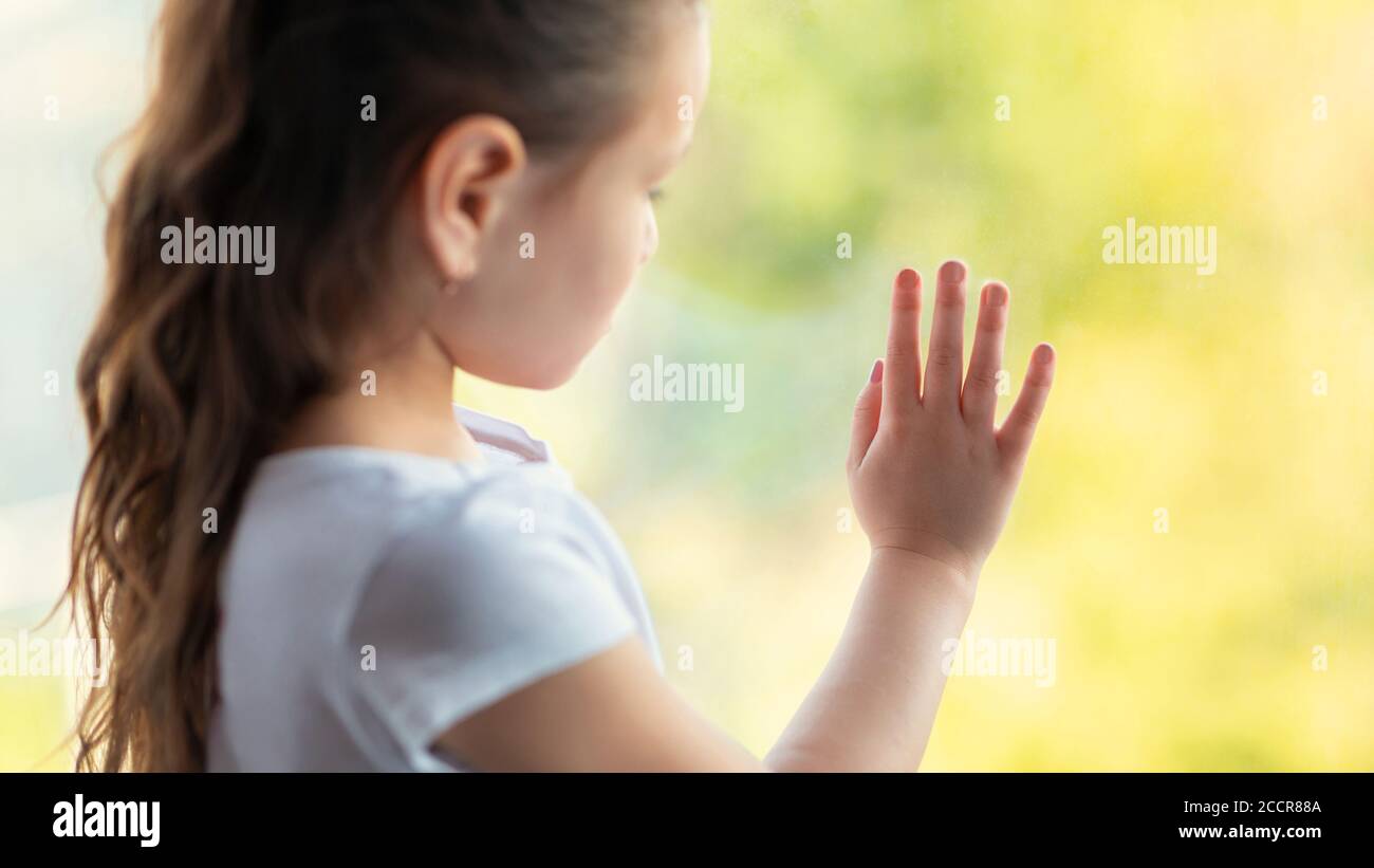 Lonely Kid Girl Standing Near Window At Home Looking Outside Stock Photo
