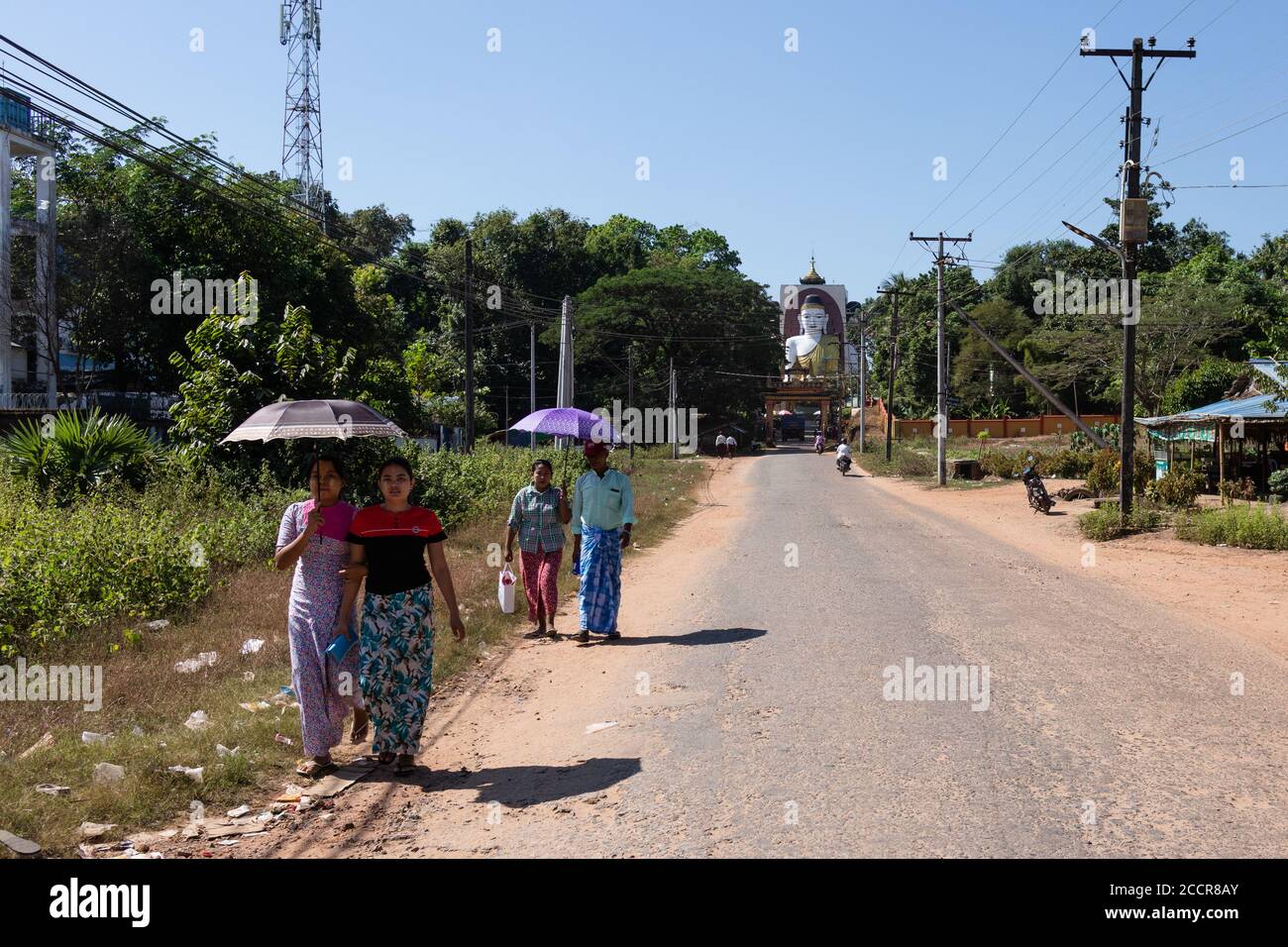 Kyaik Pun pagoda. People walking dressed in the traditional manner covering their heads from the strong sun with umbrellas. Bago, Myanmar, Burma, Asia Stock Photo