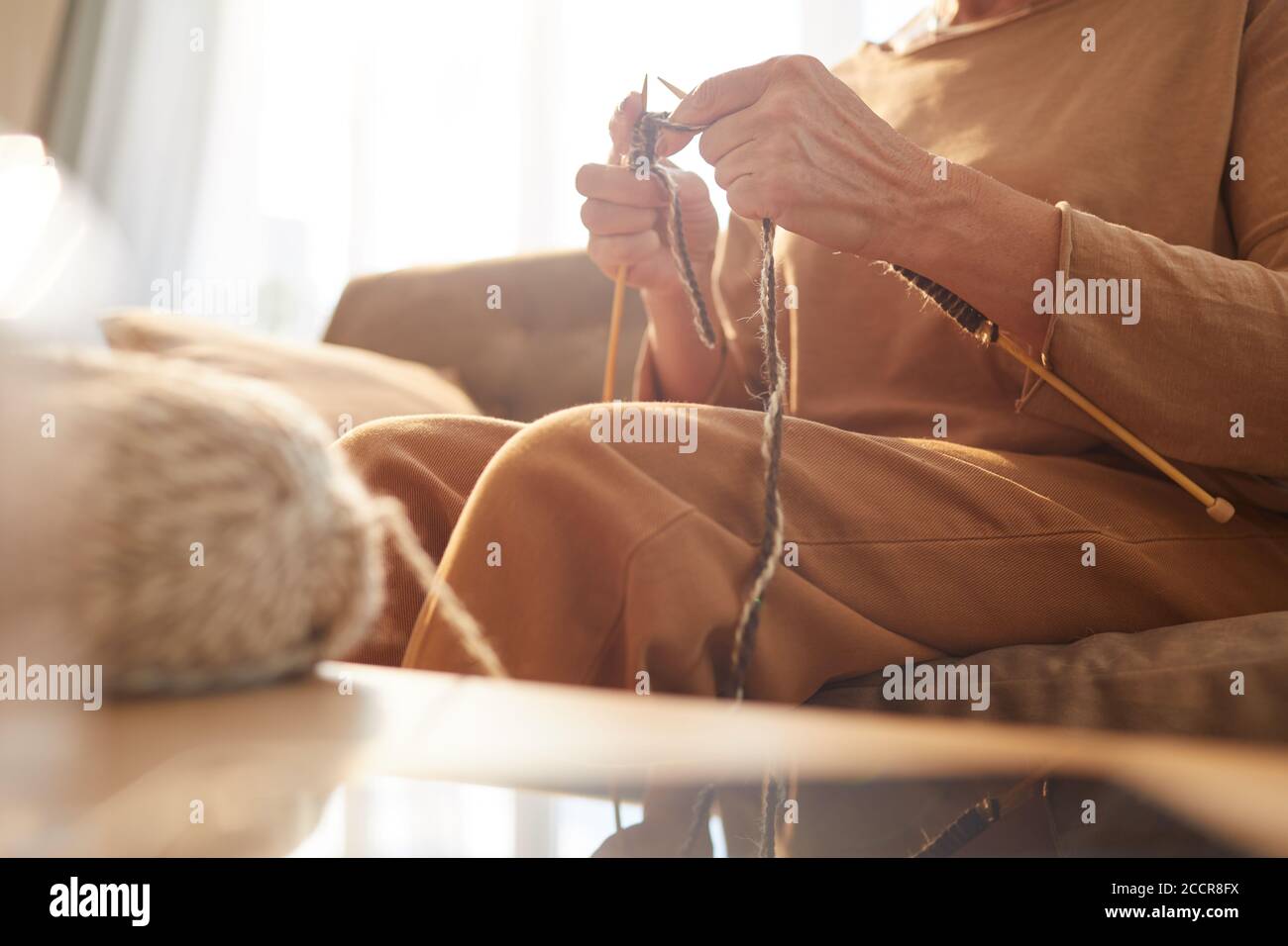 Warm toned closeup of unrecognizable senior woman knitting in cozy home ...