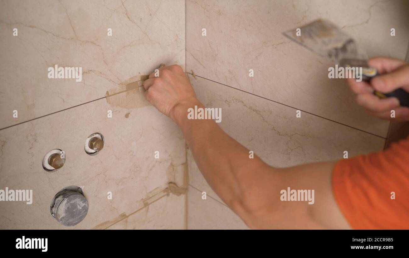 master tiler glues wall white ceramic tiles. The process of grouting the joint between tiles in