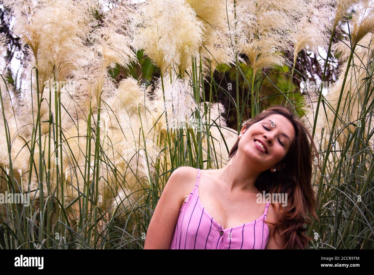 Young woman enjoying a relaxing moment into nature. Some wildflowers surround her in background. Stock Photo