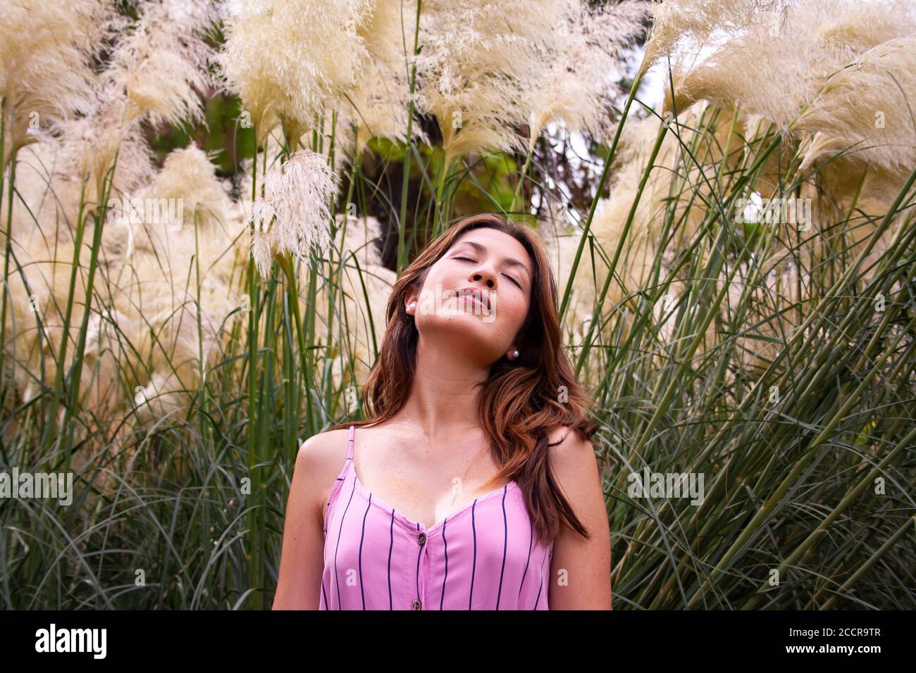 Young woman enjoying a relaxing moment into nature. Some wildflowers surround her in background. Stock Photo