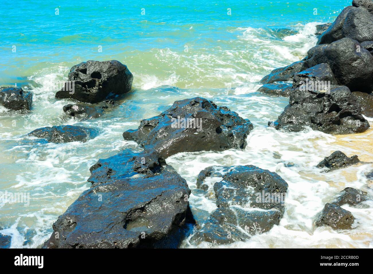 Rocks on the shore of a beautiful beach with blue water Stock Photo - Alamy