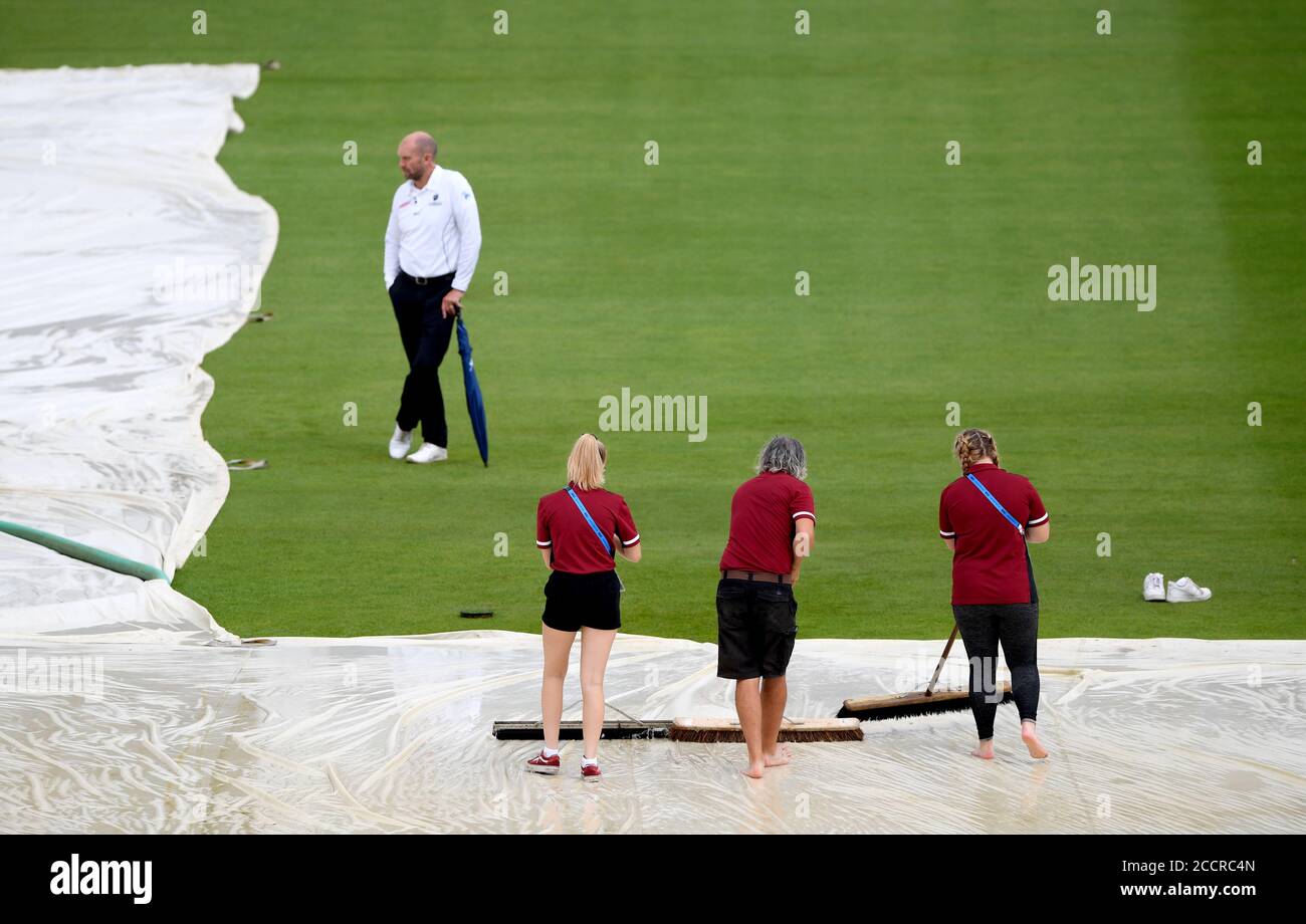 Umpire Mike Burns (top left) inspects the ground as groundstaff sweep water off the covers after heavy rain stopped during day four of the third Test match at the Ageas Bowl, Southampton. Stock Photo