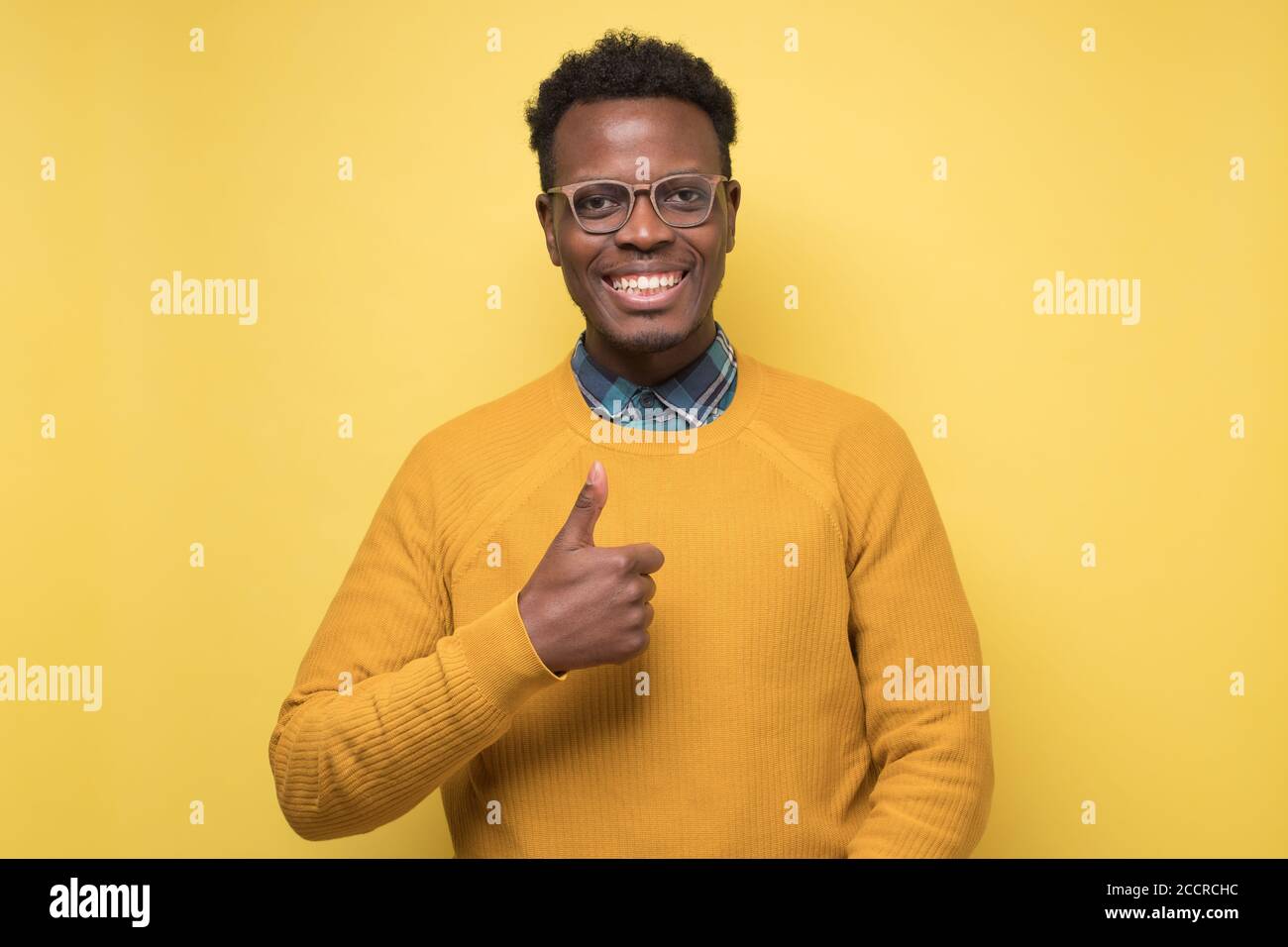 Handsome black man shoing thumb up. Studio shot on yellow wall. Stock Photo