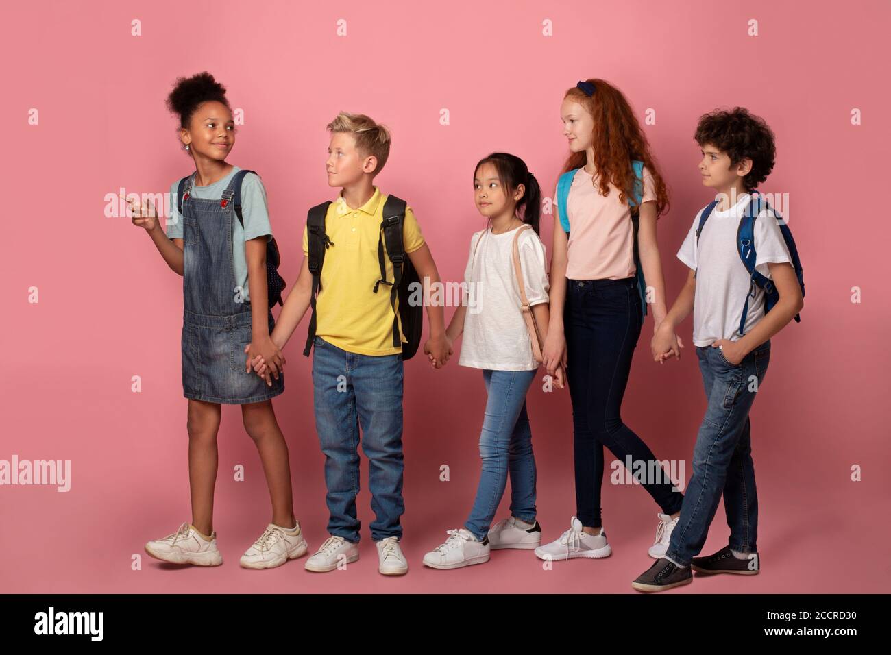 Body size portrait of schoolkids walking to school hand in hand over pink background Stock Photo