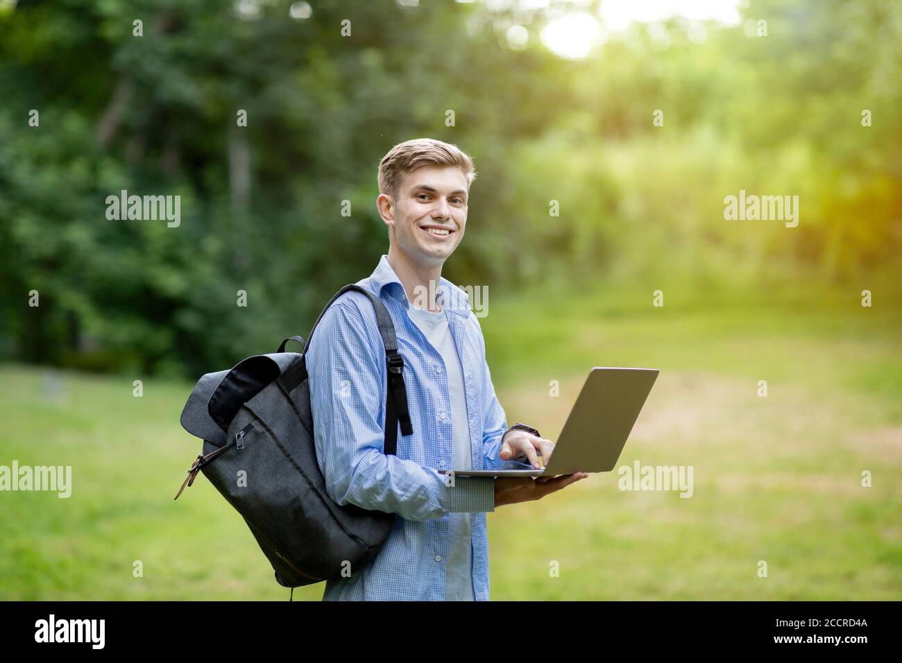 Happy student guy with laptop and backpack posing outdoors at college ...