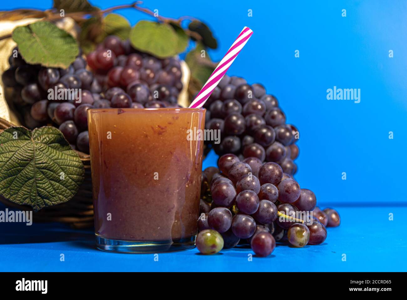 Grape juice in a glass. Bunches of grape of the niagara species (Vitis labrusca 'Niagara'). Blue background. Refreshing drink. The niagara grape is on Stock Photo