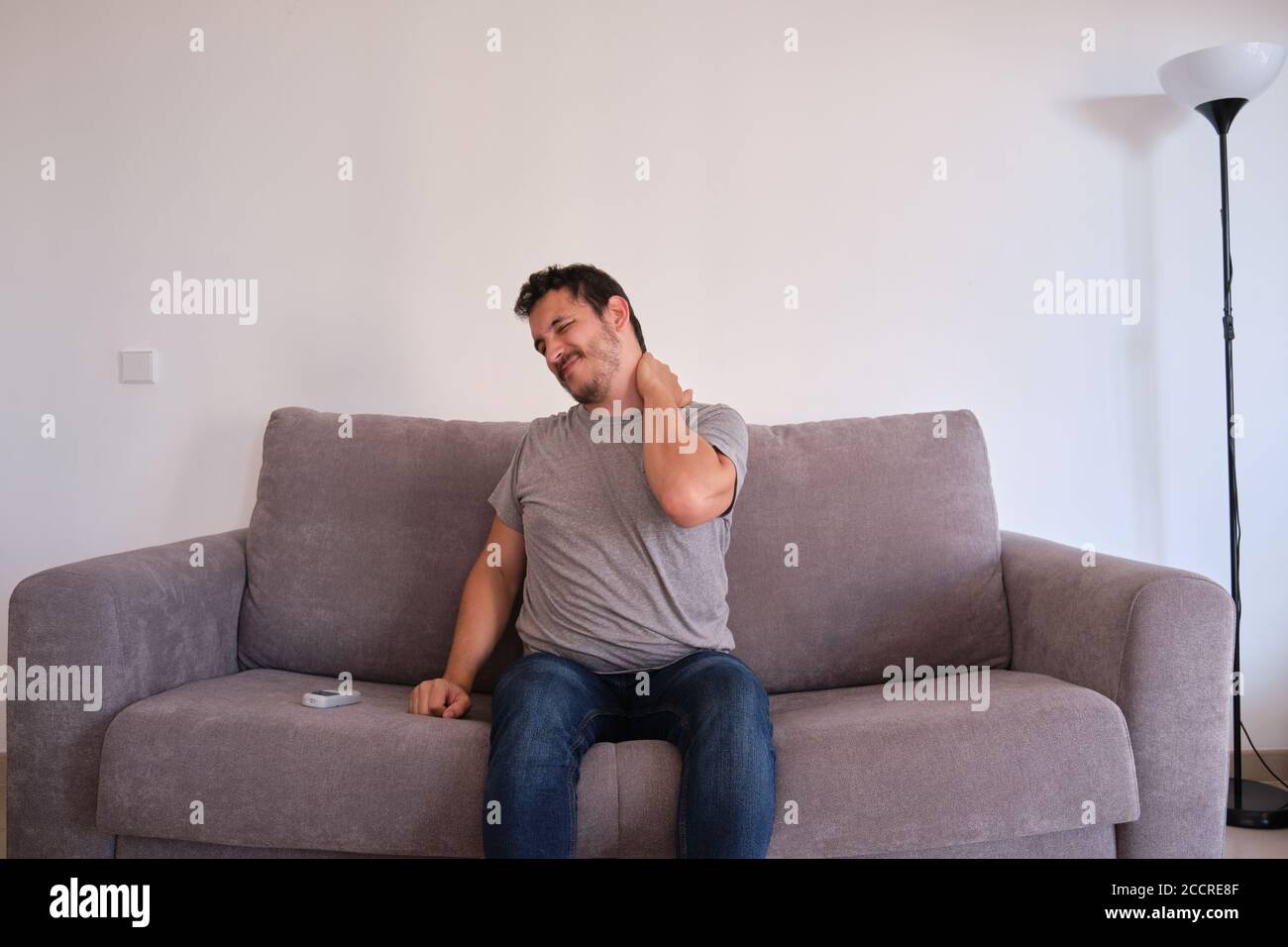 Young man sitting on a sofa suffering from neck pain. Neck and shoulder