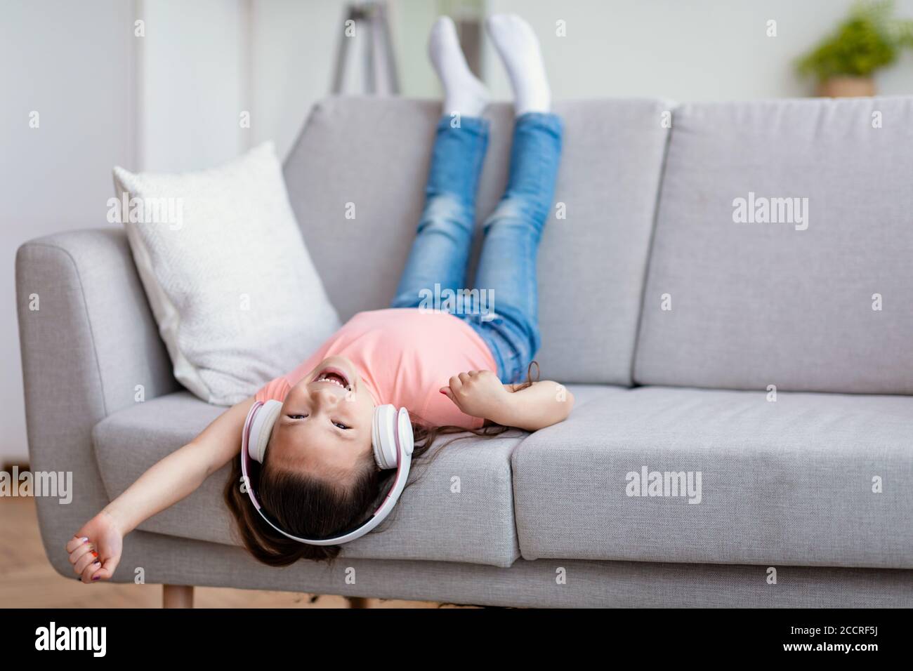 Asian Girl Wearing Headphones Sitting Upside Down On Couch Indoor Stock