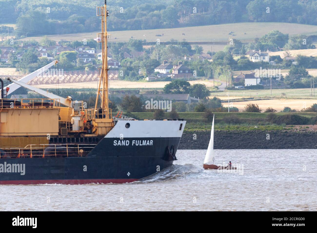 Hopper Dredger, Sand Fulmar, with bow wave passing a small vintage wooden sailing boat. Little and large, scale of different river traffic on Thames Stock Photo