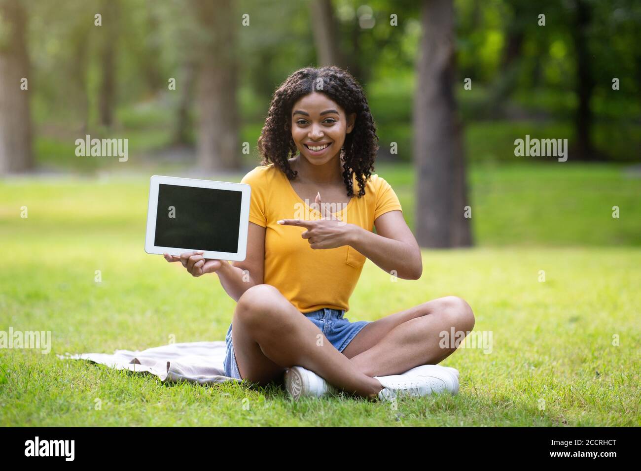 Joyful African American woman pointing at tablet computer with empty ...