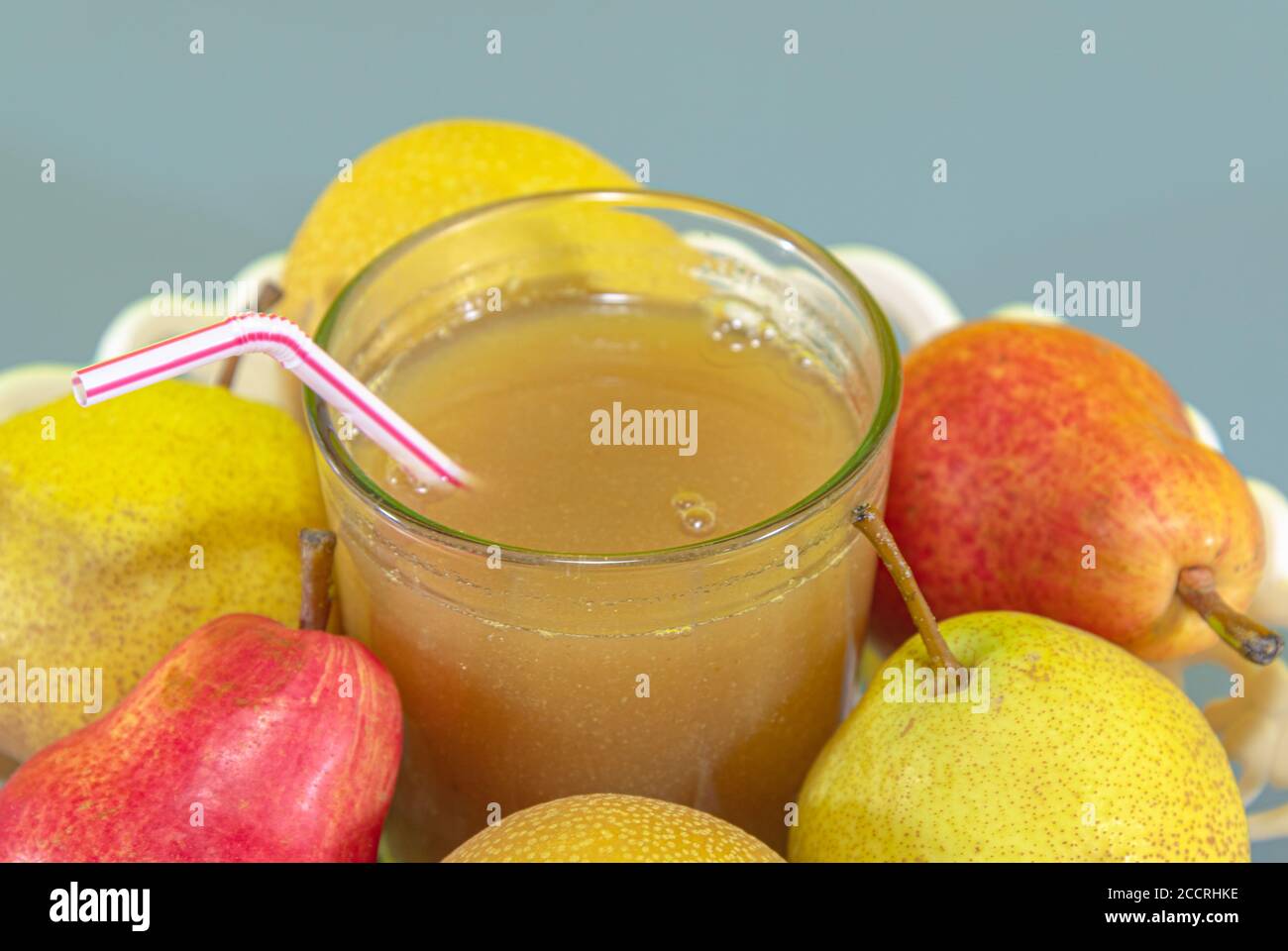 Fruit juice. Pear juice (Pyrus spp). Blue background. Energy drink rich in fiber. Antioxidant and detox drink and beverage. Fresh fruits in white tray Stock Photo