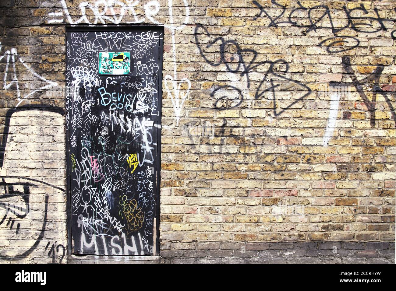 Vandalised brick wall and door background showing colourful spray paint in  an urban ghetto Stock Photo - Alamy