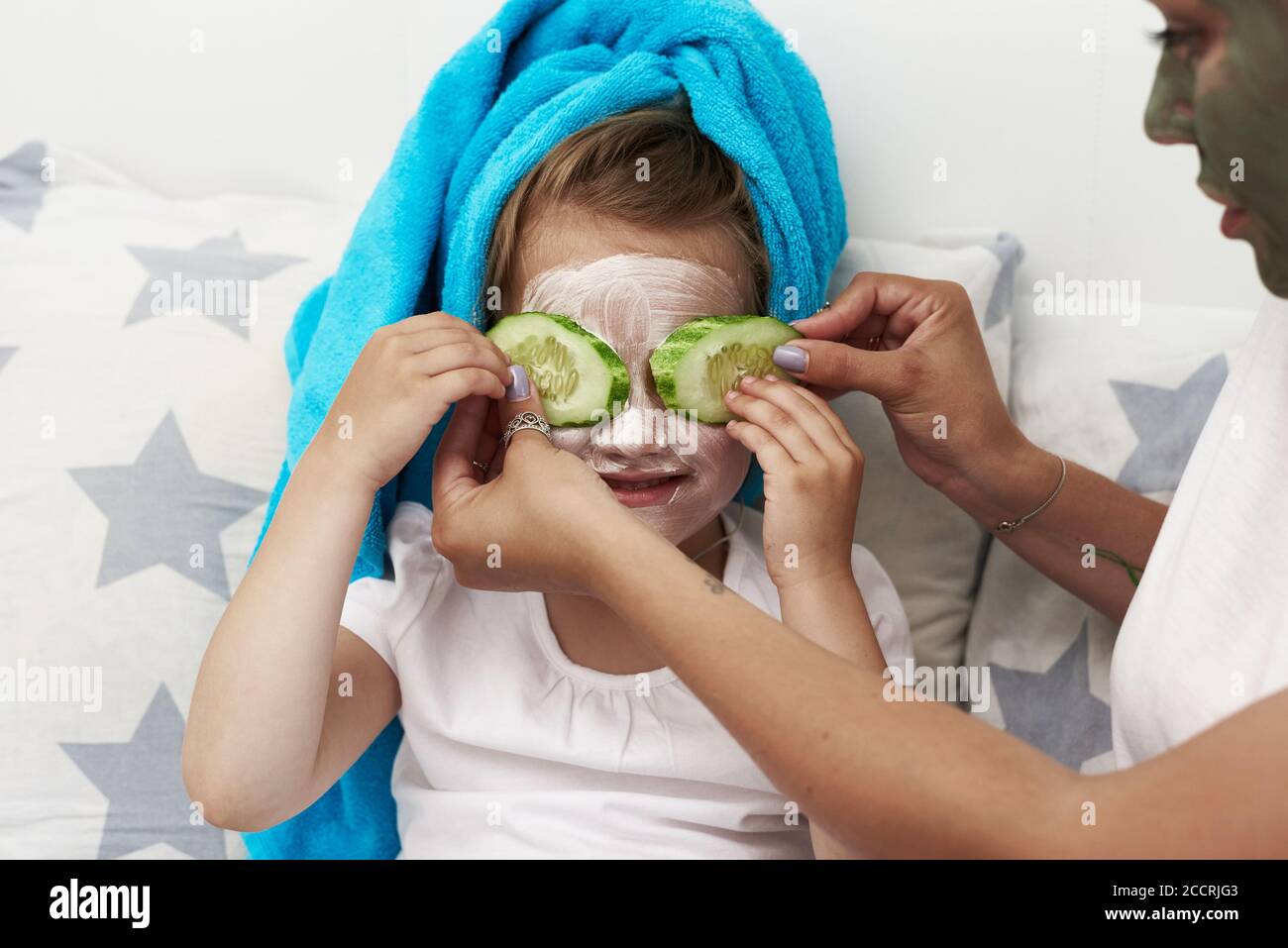 Morning care routine. Mom and daughter conduct beauty treatments. They are sitting on the couch and applying pieces of cucumber to their eyes. Stock Photo