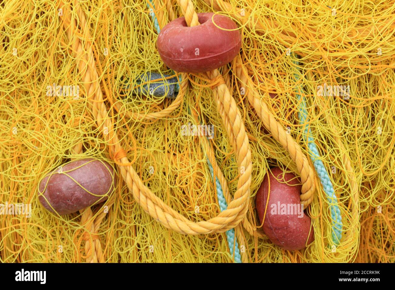 Yellow fishing netting with red buoys heaped on the harbourside Stock Photo