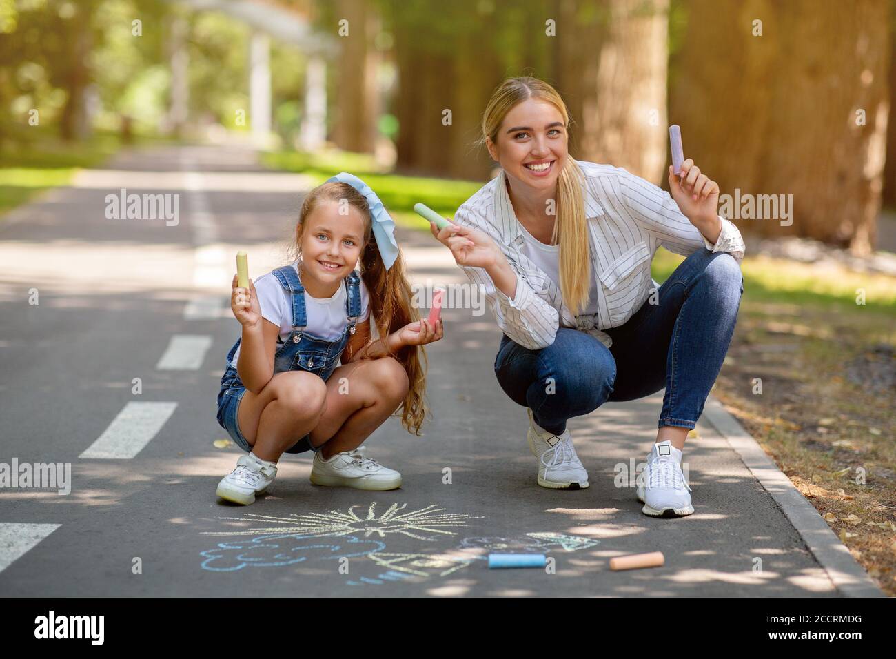 Happy Mom And Daughter Holding Colorful Chalks Drawing In Park Stock Photo