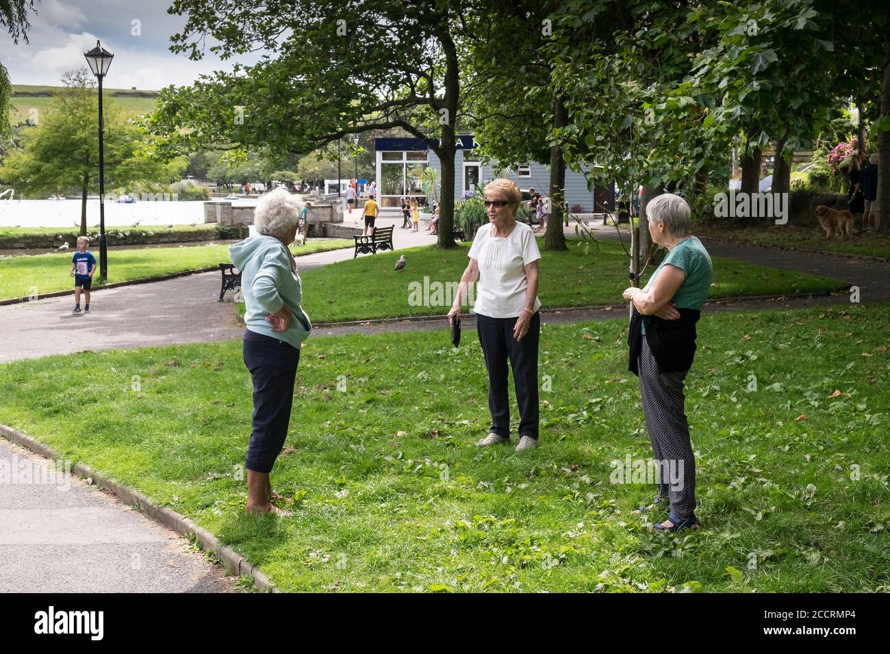 Mature female friends maintaining social distancing chatting in Trenance Gardens in Newquay in Cornwall. Stock Photo