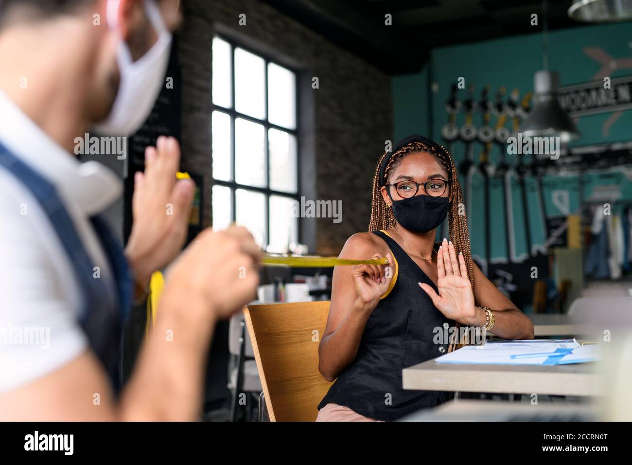 Young businesspeople with face masks working indoors in office, keeping safe distance. Stock Photo