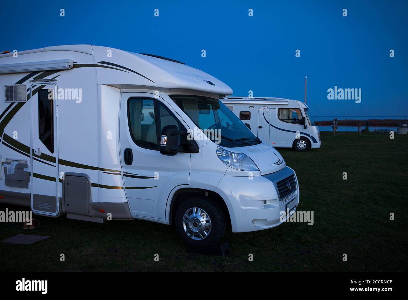 Two motorhomes parked at a campsite in the evening. Stock Photo