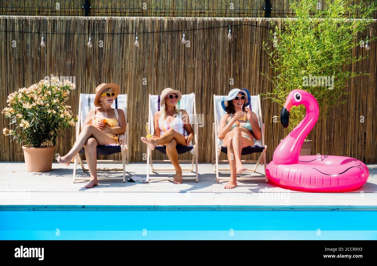 Group of cheerful women seniors sitting by swimming pool outdoors in backyard. Stock Photo