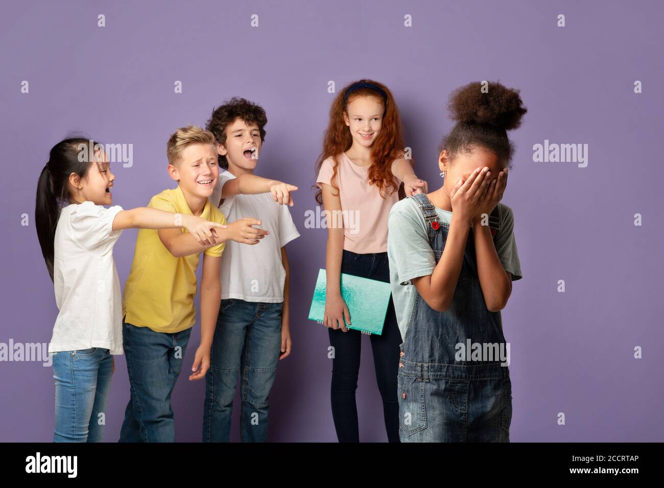 Group of schoolkids bullying their crying African American classmate over lilac background Stock Photo